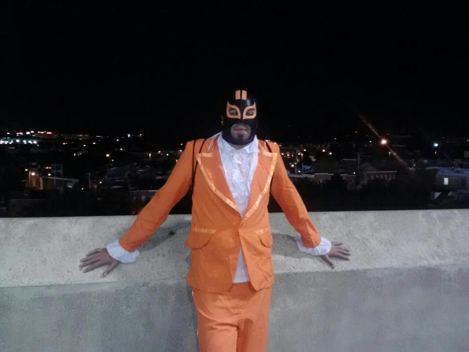 oriole fan with orange suit and face mask posing in front of concrete barrier
