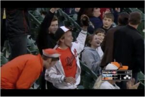 guy in stands holding up glove with baseball in it