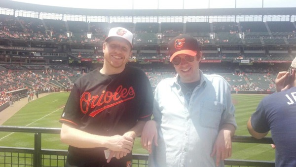 two guys leaning up against railing for picture at orioles game