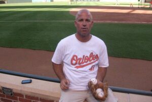 orioles player matt hersl sitting on ledge with glove and three baseballs