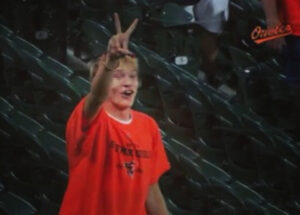 fan in stands arm up showing peace sign in orange shirt