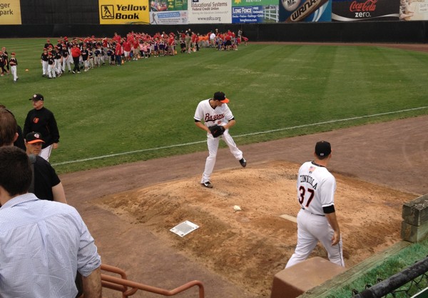 pitcher practicing with group of kids walking on baseball field