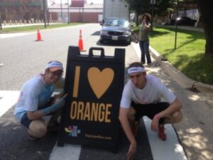 two guys kneeling down by street sign that says i heart orange