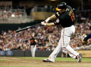 orioles player about to hit baseball from home plate with blurred crowd in background