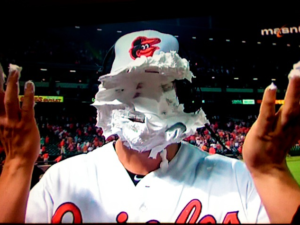 person with pie all over face wearing orioles hat and jersey