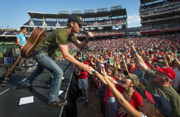 country singer on stage singing during playoff game with fans holding hands out