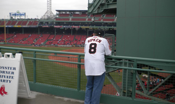 guy leaning against fence in cal ripken jersey at fenway park
