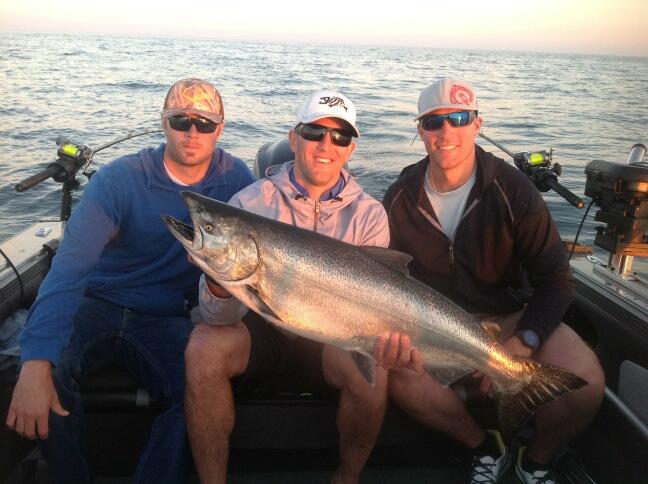 three baseball players on off day on boat next to each other holding up salmon caught