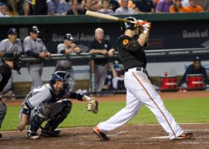 orioles player at bat with yankees catcher behind him after hitting ball