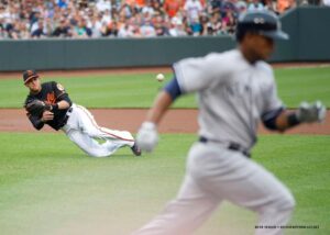 orioles player diving to catch ball while yankees player is running by