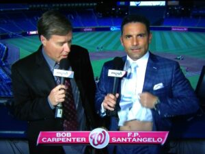 two sports broadcasters for baseball one holding bottom of shirt up