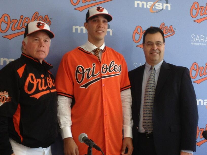 orioles player standing between two men at press conference