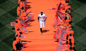 orioles player running down orange strip while fans hold orioles flags on sideline