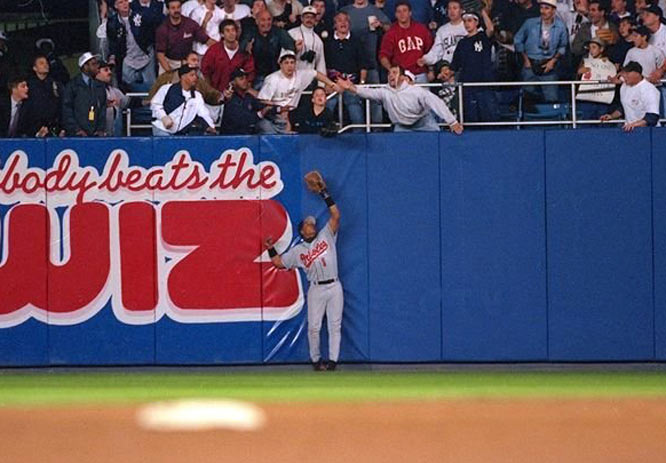 orioles player up against wall by stands trying to catch baseball