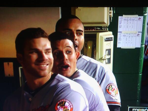 three orioles players standing in dugout looking behind shoulders smiling