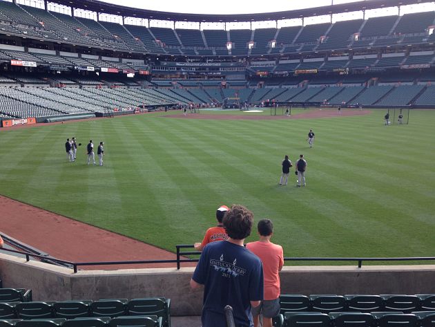 view behind three fans in stands looking out to players in field