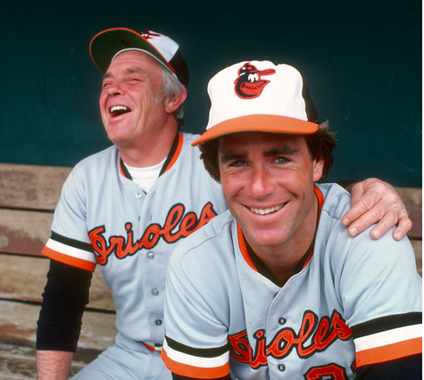 two orioles players sitting on bench one with hand on others shoulder