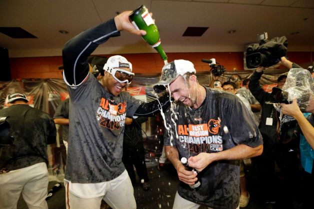 oriole player pouring champagne over anothers head with reporters around