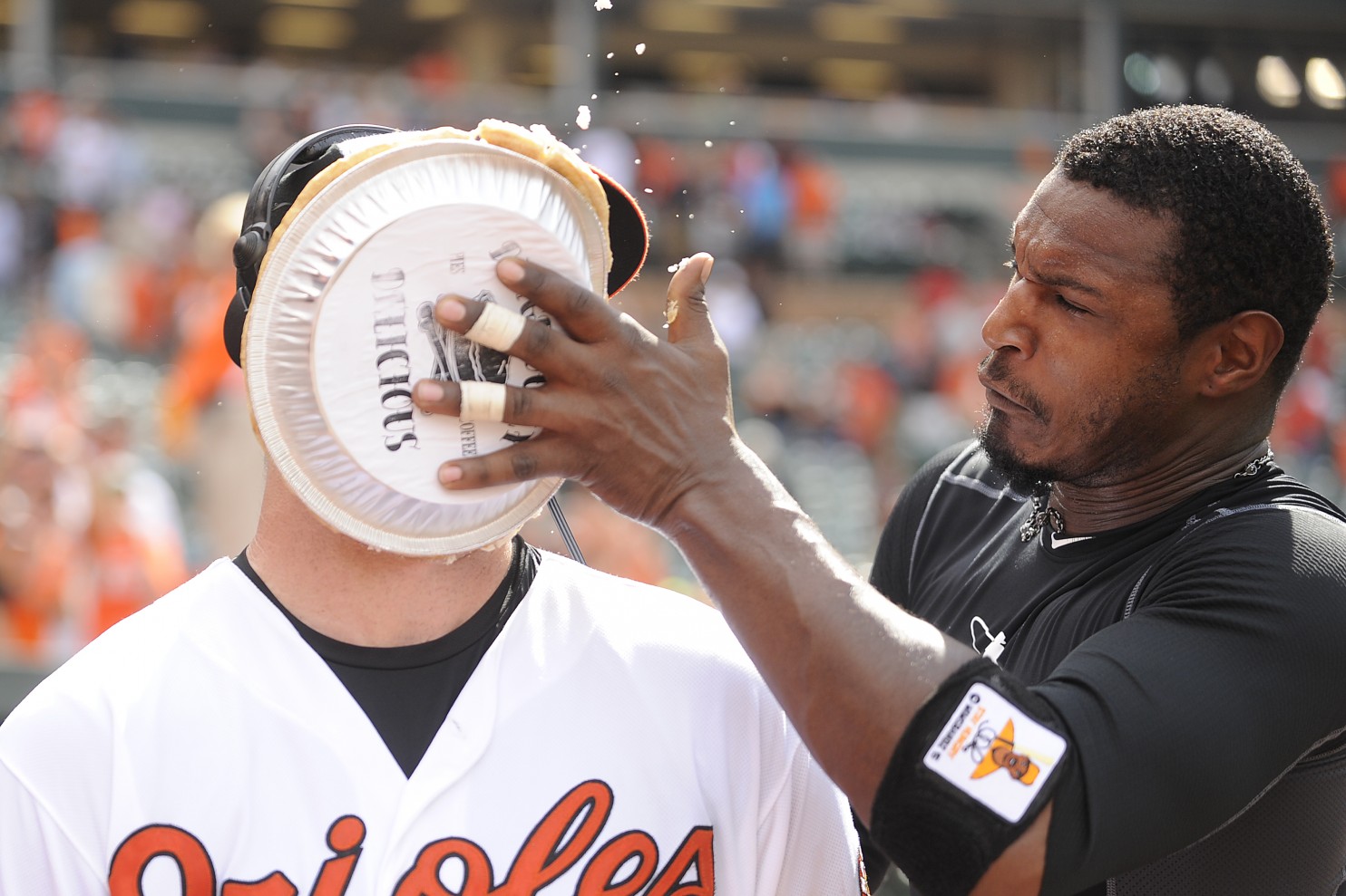 baseball player with pie in face by other team members hand