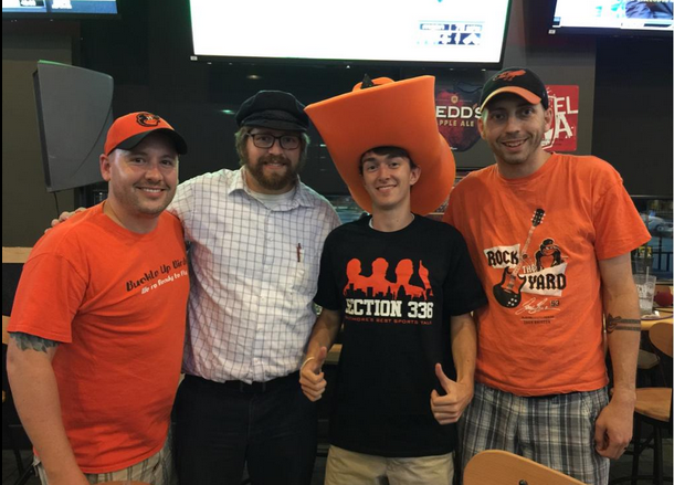 four guys posed with orioles gear on in front of flat screens