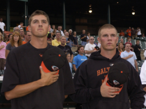 Kevin Gausman and Dylan Bundy stand side by side with their caps off and held to their chests.