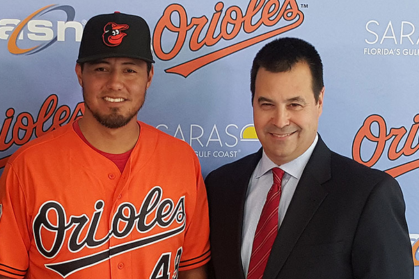 A man in an Orioles uniform and a man in a business suit stand side by side.