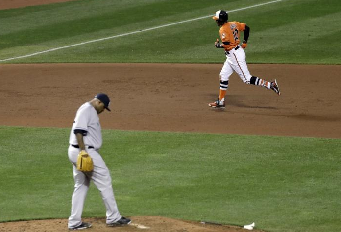 A baseball player rounds the bases while the pitcher kicks the rubber.