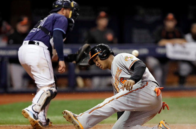 An Orioles player slides into home while a Rays catcher catches the ball.