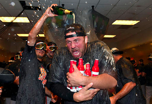 Tommy Hunter holds an armful of beers as a teammate dumps champagne on his head.